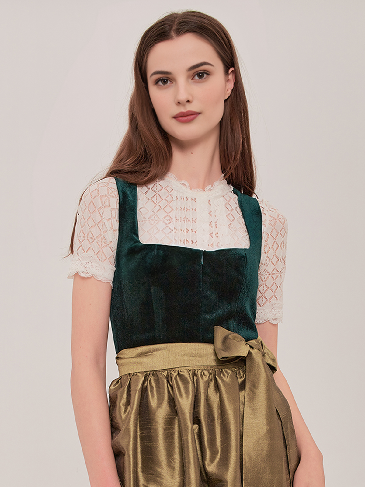 Ein grünes kurzes Dirndl mit weißer Bluse und passendem Schmuck
